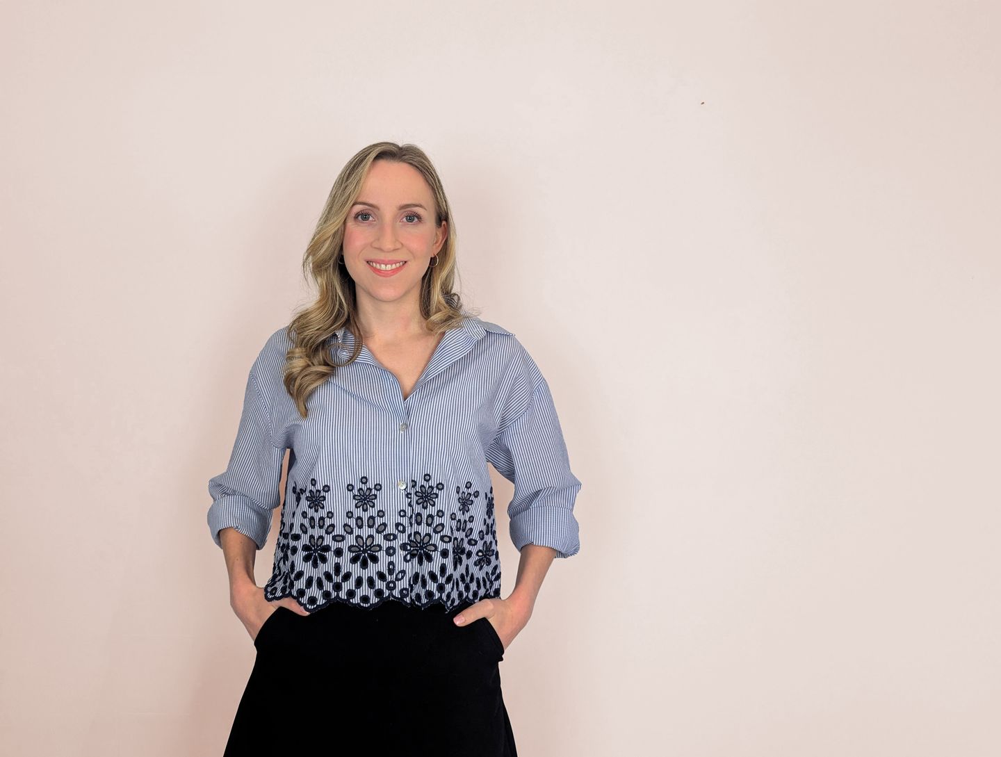 Nina Bonifazi steht lächelnd vor einer rosa Wand, die Hände in den Hosentaschen